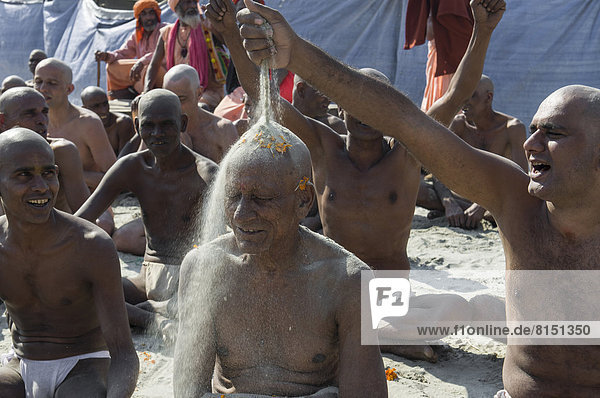 Mann gießt Sand über den Kopf eines anderen Mannes bei der Initiierung neuer Sadhus  während des Kumbha Mela Festivals
