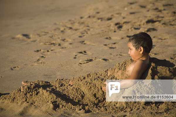 Junge vergräbt sich im Sand am Strand