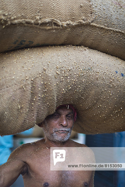 Älterer Mann trägt zwei mit Gewürzen gefüllte Säcke auf dem Kopf