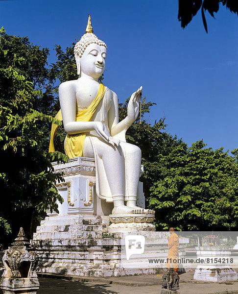 Mönch vor einer weißen sitzenden Buddha-Statue im Wat Mahathat  Geschichtspark Sukhothai