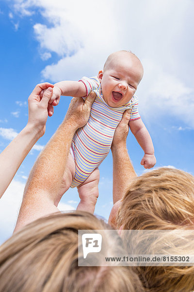 Father holding baby boy up in air against sky