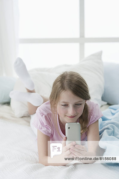Mädchen mit Smartphone im Bett  lächelnd