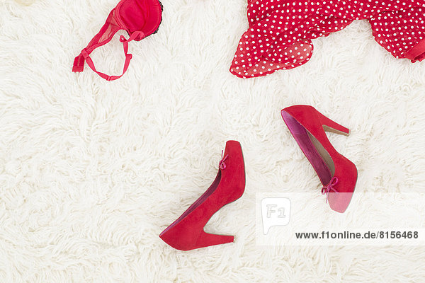 Rote High Heels und rote Innenbekleidung liegen auf weißem Teppich