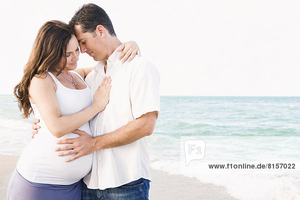 Caucasian man hugging pregnant wife on beach