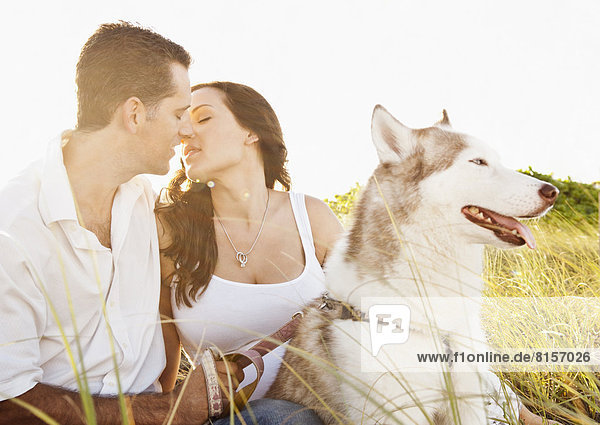Caucasian couple sitting with dog in tall grass