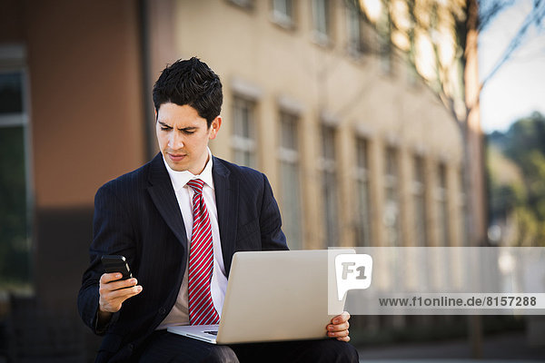 Hispanic businessman using laptop and cell phone