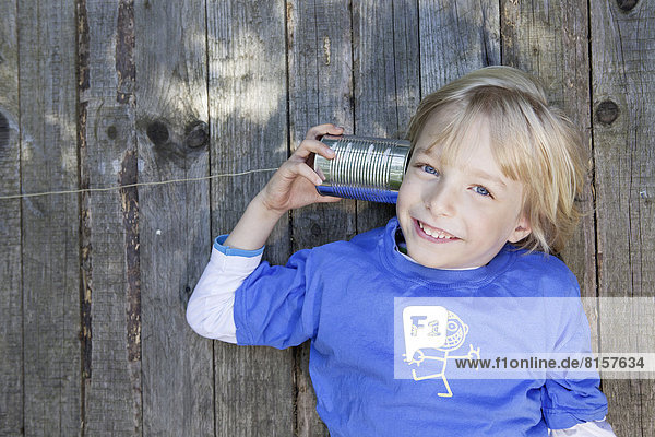 Deutschland  Nordrhein-Westfalen  Köln  Porträt eines Jungen  der Blechdosentelefon hört  lächelnd