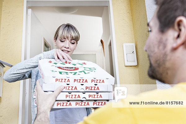 Germany  North Rhine Westphalia  Cologne  Young woman taking pizza boxes from delivery man  smiling