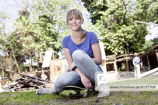 Deutschland  Nordrhein-Westfalen  Köln  Mutter sitzend auf dem Skateboard  Sohn stehend im Hintergrund