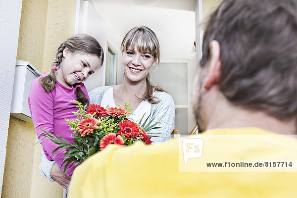 Deutschland  Nordrhein-Westfalen    Mutter und Tochter nehmen Blumen vom Briefträger  lächelnd