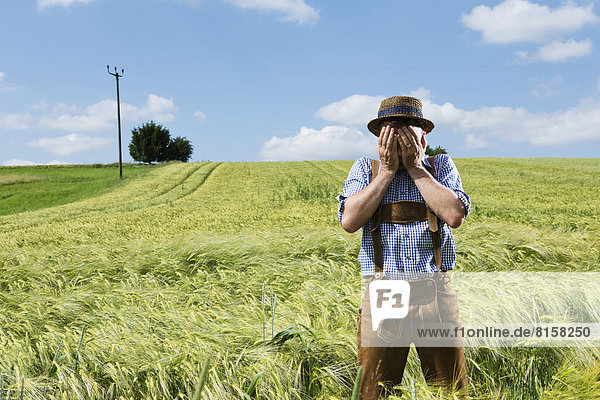 Germany  Bavaria  Farmer covering his face in field