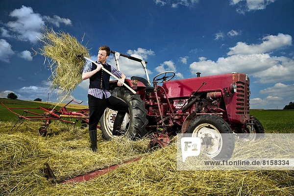 Deutschland Bayern Landwirt mit Rechen im Feld