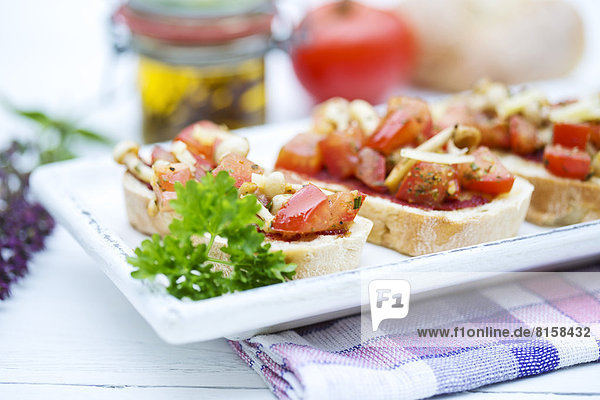 Bruschetta-Teller mit Tomaten  weißen Shimeji-Pilzen  Kräutern und Olivenöl auf Holztisch  Nahaufnahme