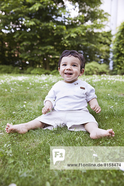 Baby boy sitting on grass and holding daisy flower  smiling