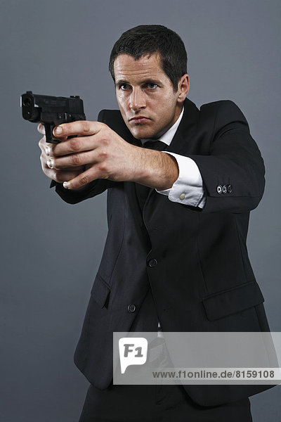 Mature man aiming handgun against grey background