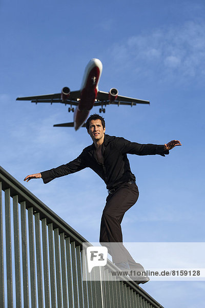 Mittelgroßer Mann am Geländer mit Landeflugzeug im Hintergrund