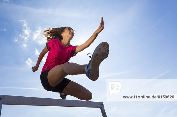 Germany  Young woman athlete jumping hurdles on track