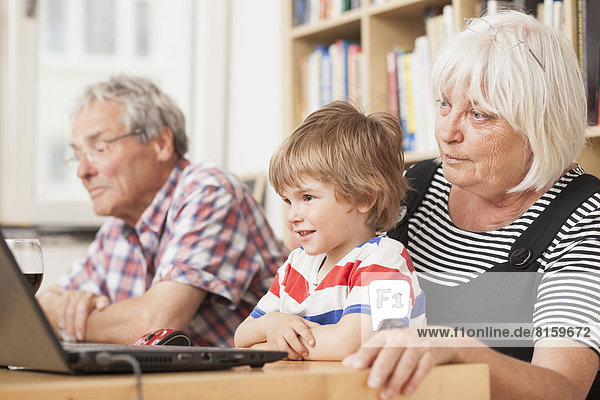 Germany  Berlin  Grandparents and grandson using laptop  smiling