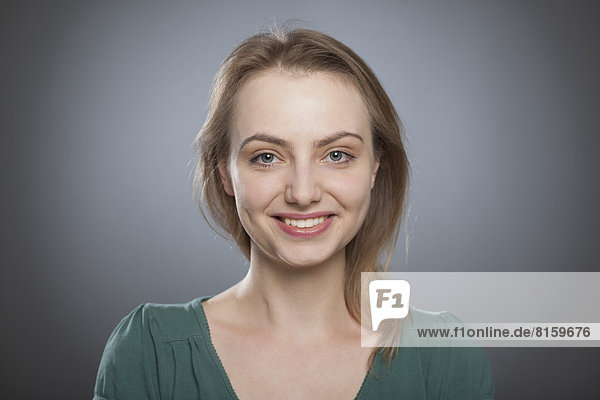 Porträt einer jungen Frau vor grauem Hintergrund  lächelnd