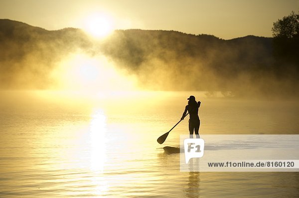 A woman  is silhouetted Stand Up Paddleboarding (SUP) at sunrise in the mist in Lake Tahoe  CA.