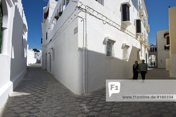 A man and woman walk down a street in the coastal town of Asilah  Morocco.