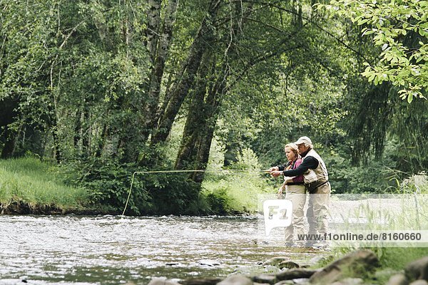 A father and daughter fly fishing on a small river for trout along the Oregon coast.