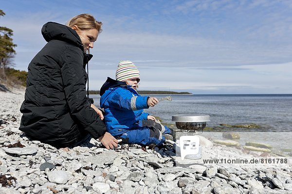 Mother with son cooking on rocky beach