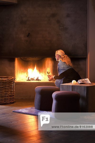 Woman sitting with wineglass and looking at fireplace