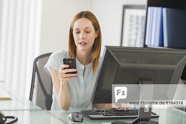 Business woman using computer and phone in office