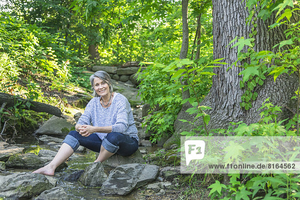Senior woman sitting on rock in forest