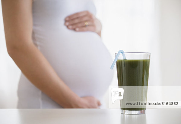 Mid section of pregnant woman  green smoothie in front