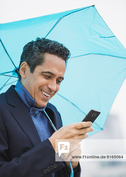 Portrait of man holding blue umbrella and using mobile phone