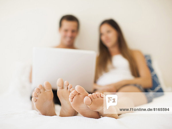 Couple lying on bed with laptop