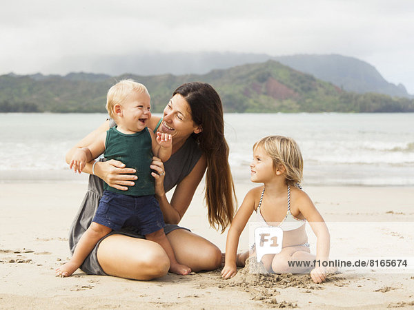 Mother playing with daughters (6-11 months  2-3) on beach