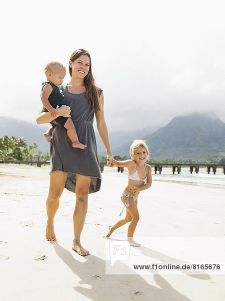 Mother walking with daughters (6-11 months  2-3) on beach