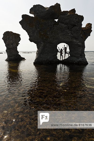Two kids playing in natural arch of sea rock