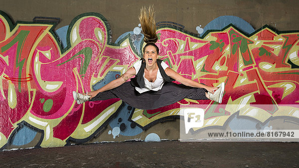 Hip-Hop-Tänzerin im Sprung vor einer Wand mit Graffiti