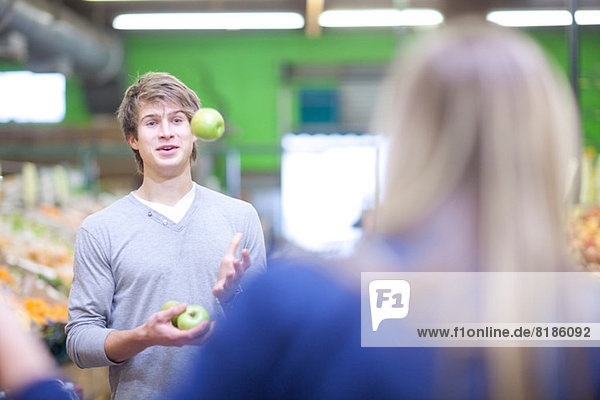 Junger Mann jongliert mit Äpfeln im Indoor-Markt