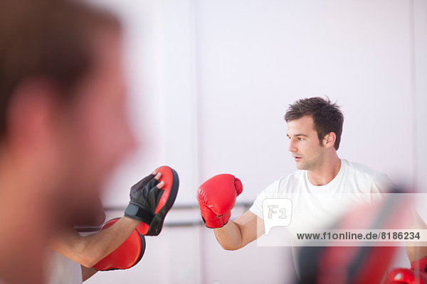 Young man and trainer boxing in sports hall