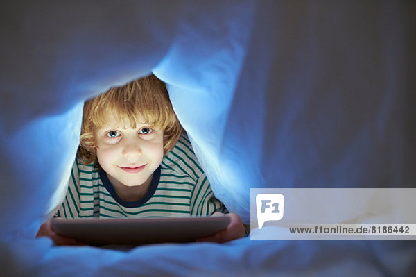 Junge unter der Bettdecke mit digitalem Tablett