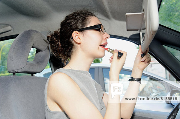 Junge Frau beim Auftragen von Lippenstift im Auto Mund