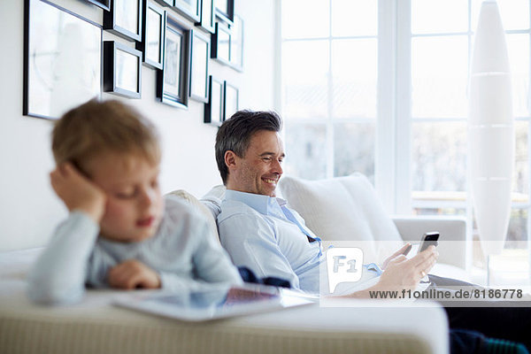 Vater und Sohn sitzen auf dem Sofa mit digitalem Tablett und Smartphone