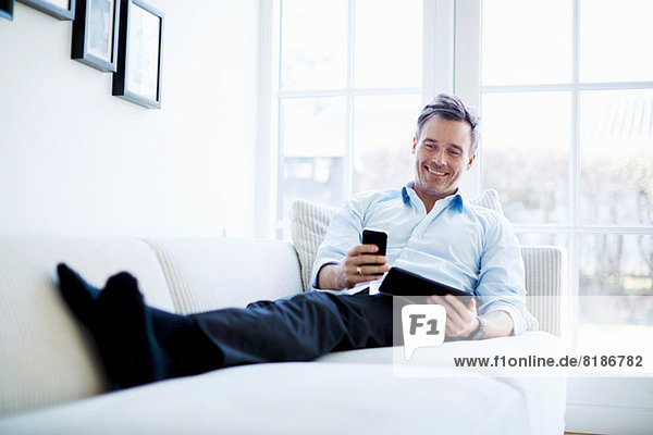 Mann entspannt auf dem Sofa mit digitalem Tablett und Smartphone