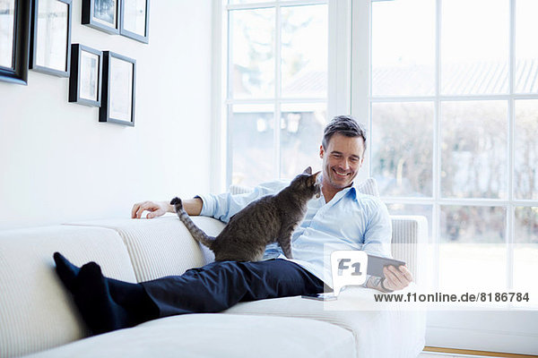 Mann entspannt auf dem Sofa mit digitalem Tablett mit Katze