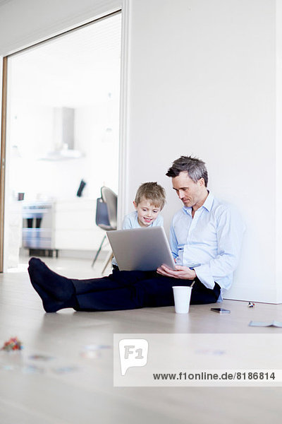 Mann auf dem Boden sitzend mit Laptop  Sohn schauend