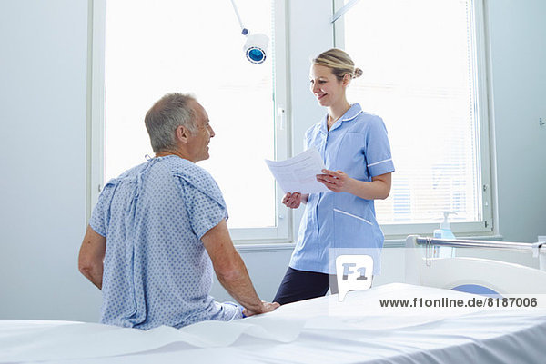 Nurse standing talking to patient sitting on hospital bed