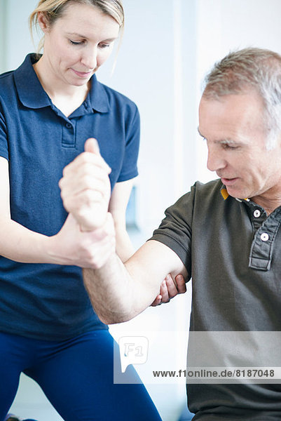Physiotherapeutin hilft dem Mann bei der Armgymnastik