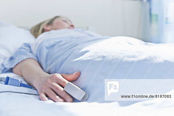 Patient liegt auf Krankenhausbett mit Monitor am Finger
