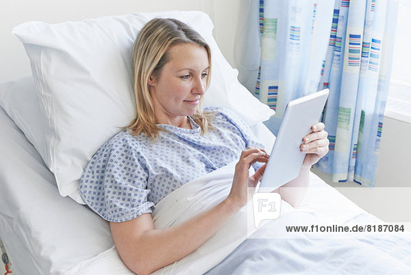 Patient lying on hospital bed using digital tablet