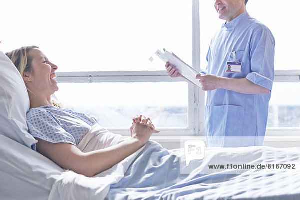 Patientin liegt im Krankenhausbett und lacht mit Krankenschwester